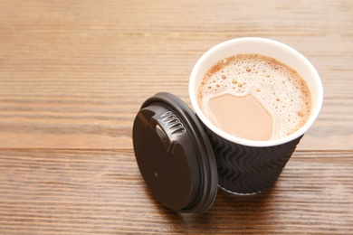 Photo of Cardboard cup of coffee on wooden table. Space for text