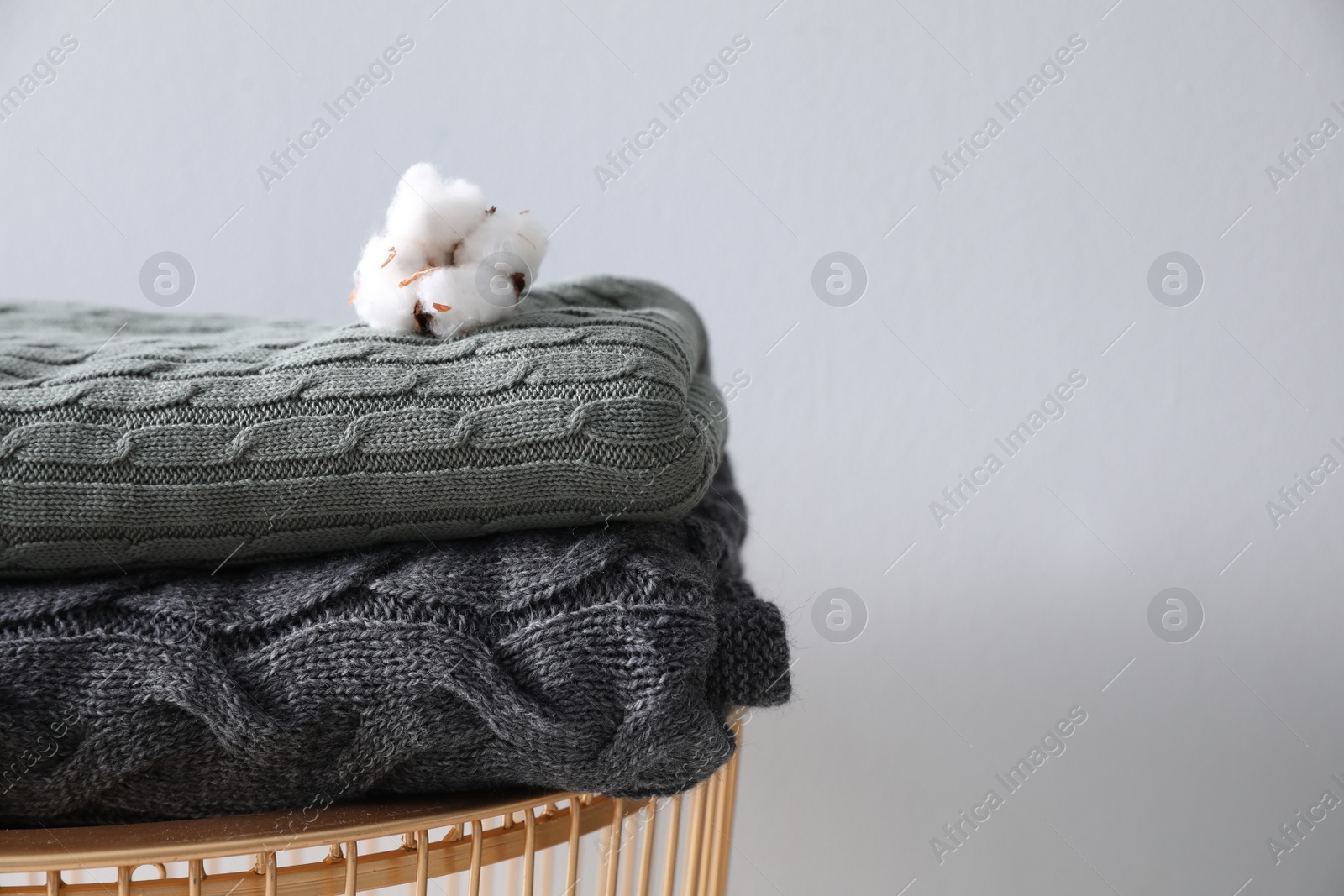 Photo of Folded soft blankets and cotton flower on coffee table near light wall, closeup. Home interior