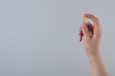 Photo of Woman holding vitamin capsule on grey background, closeup with space for text. Health supplement