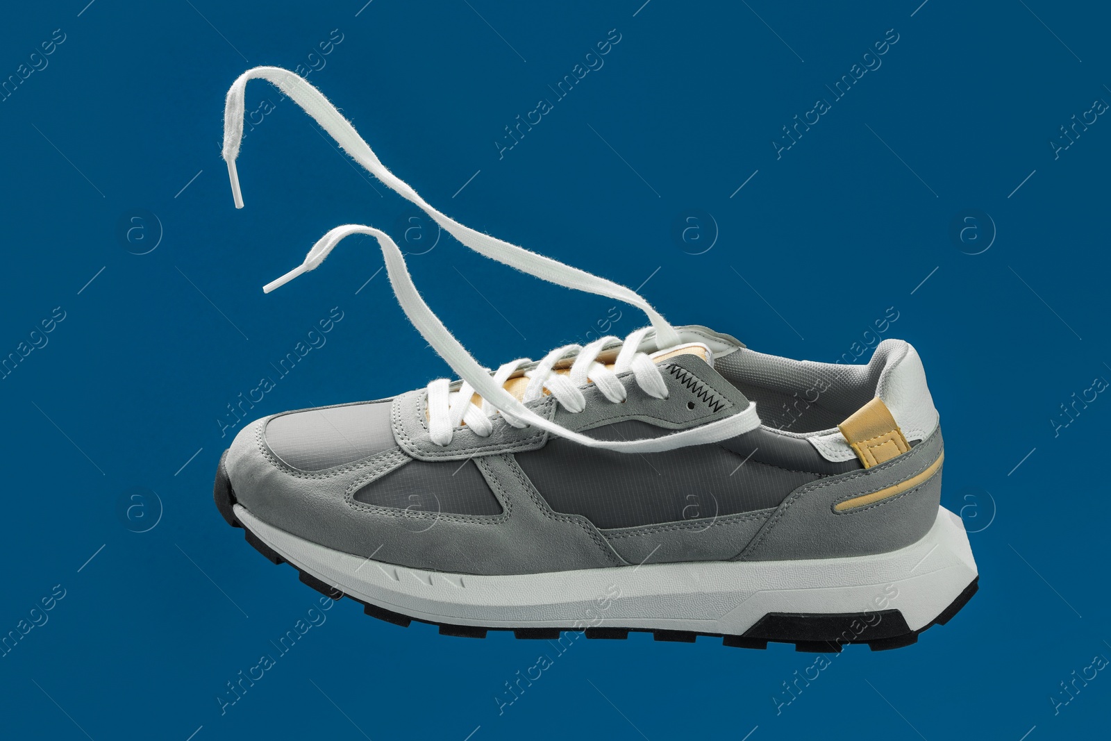 Photo of One stylish grey sneaker in air against blue background