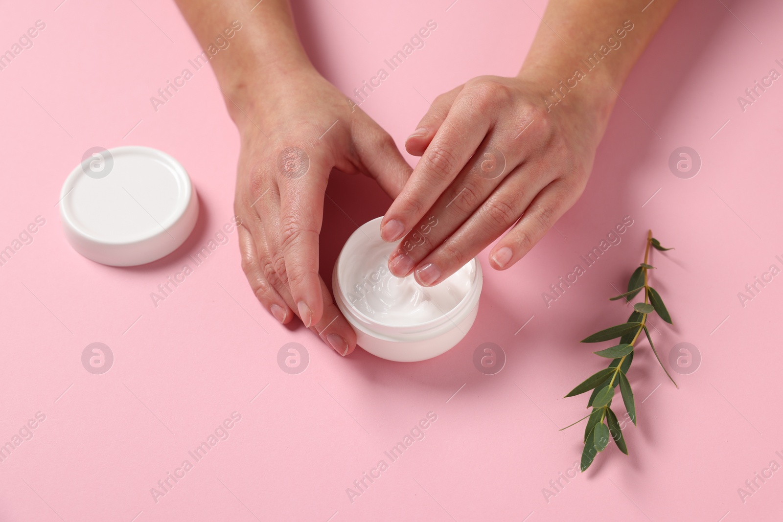 Photo of Woman with jar of hand cream and leaves on pink background, above view