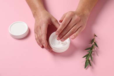 Woman with jar of hand cream and leaves on pink background, above view