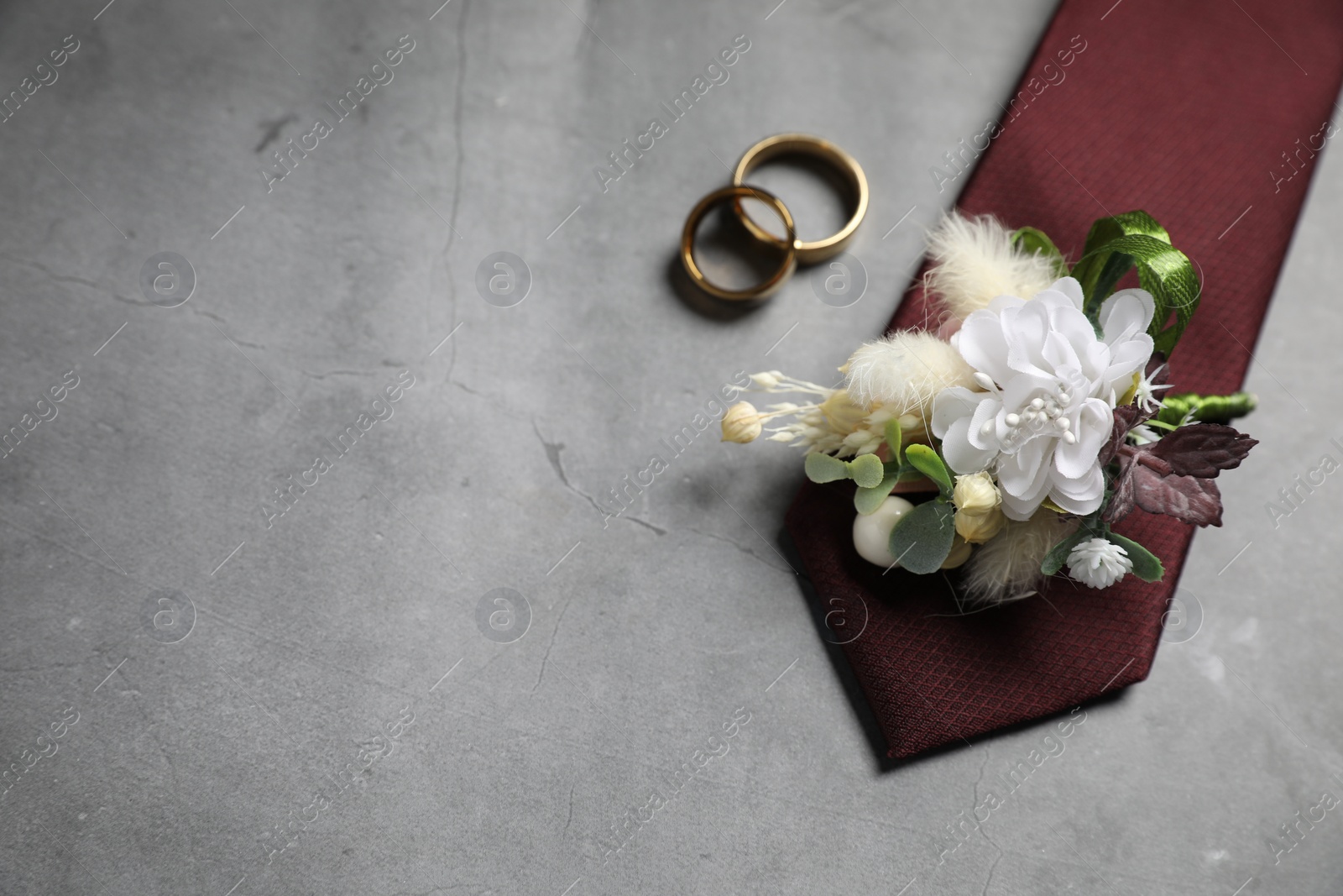 Photo of Wedding stuff. Stylish boutonniere, tie and wedding rings on gray background, flat lay. Space for text