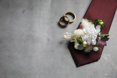 Wedding stuff. Stylish boutonniere, tie and wedding rings on gray background, flat lay. Space for text