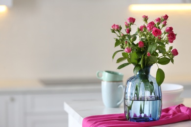 Photo of Glass vase with fresh flowers and towel on table in kitchen. Space for text