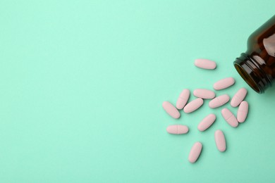 Vitamin pills and bottle on mint color background, top view. Space for text