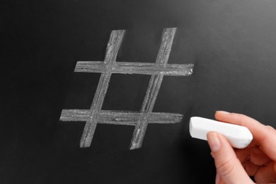 Woman drawing hashtag symbol with chalk on blackboard, closeup