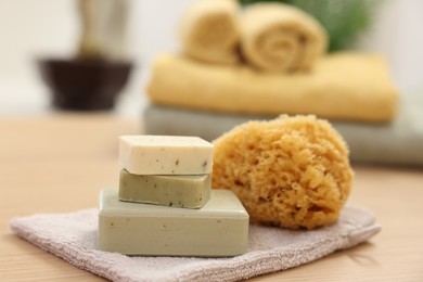 Photo of Soap bars and natural sponge on light wooden table, closeup. Spa therapy