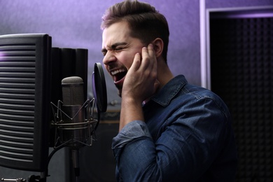 Young singer with microphone recording song in studio