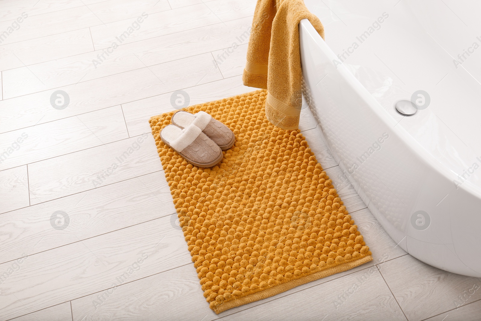 Photo of Soft orange bath mat and slippers on floor in bathroom