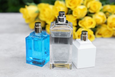 Perfumes and beautiful bouquet of yellow roses on light table, selective focus