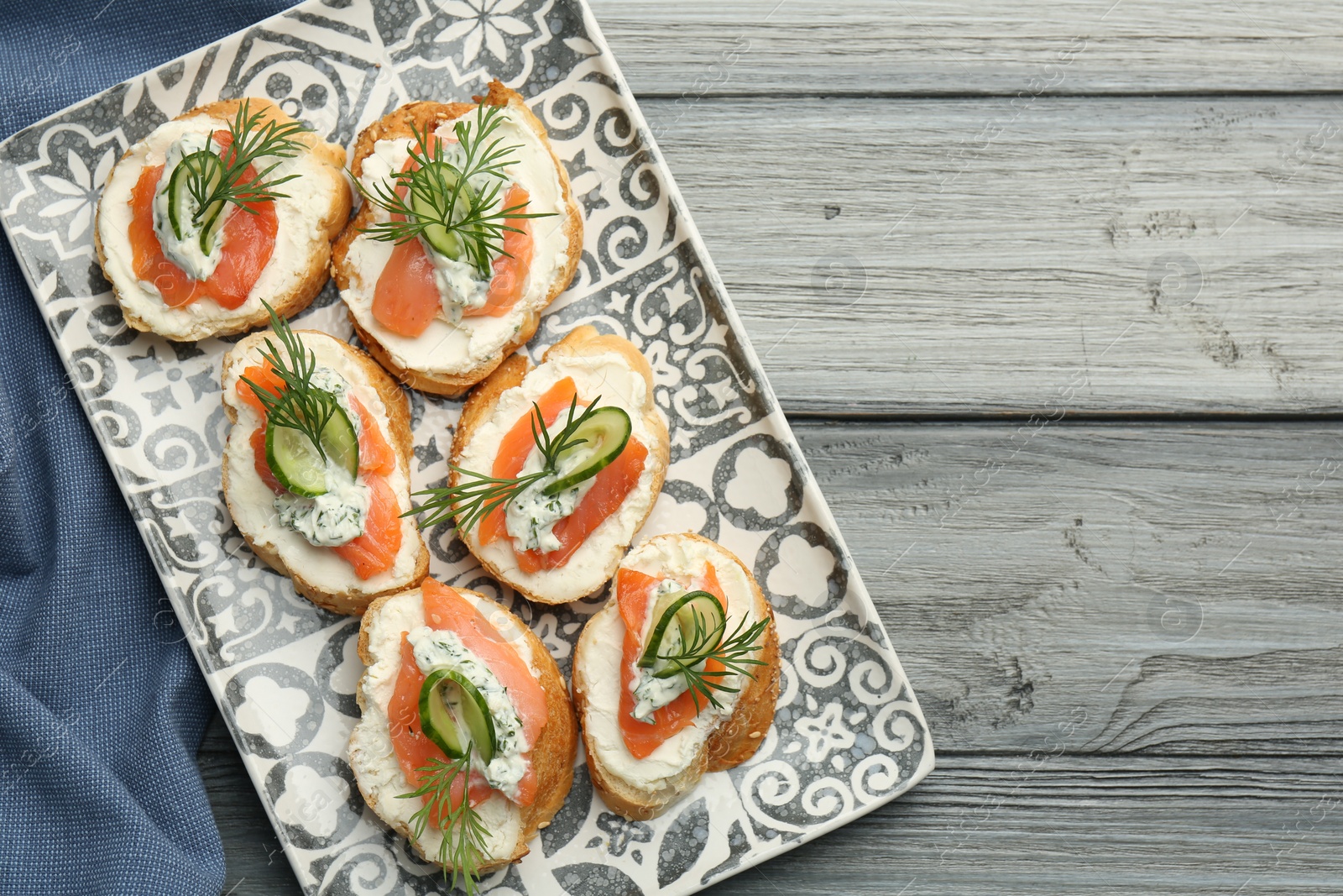 Photo of Tasty canapes with salmon, cucumber, cream cheese and dill on wooden table, top view. Space for text