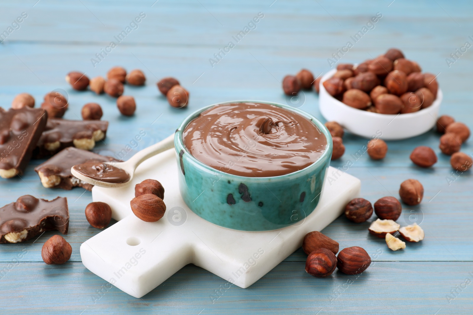 Photo of Bowl with tasty paste, chocolate pieces and nuts on light blue wooden table