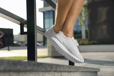 Photo of Man in stylish sneakers sitting on railing outdoors, closeup