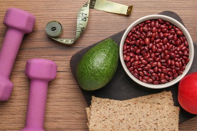 Healthy diet. Measuring tape, dumbbells and products on wooden table, flat lay