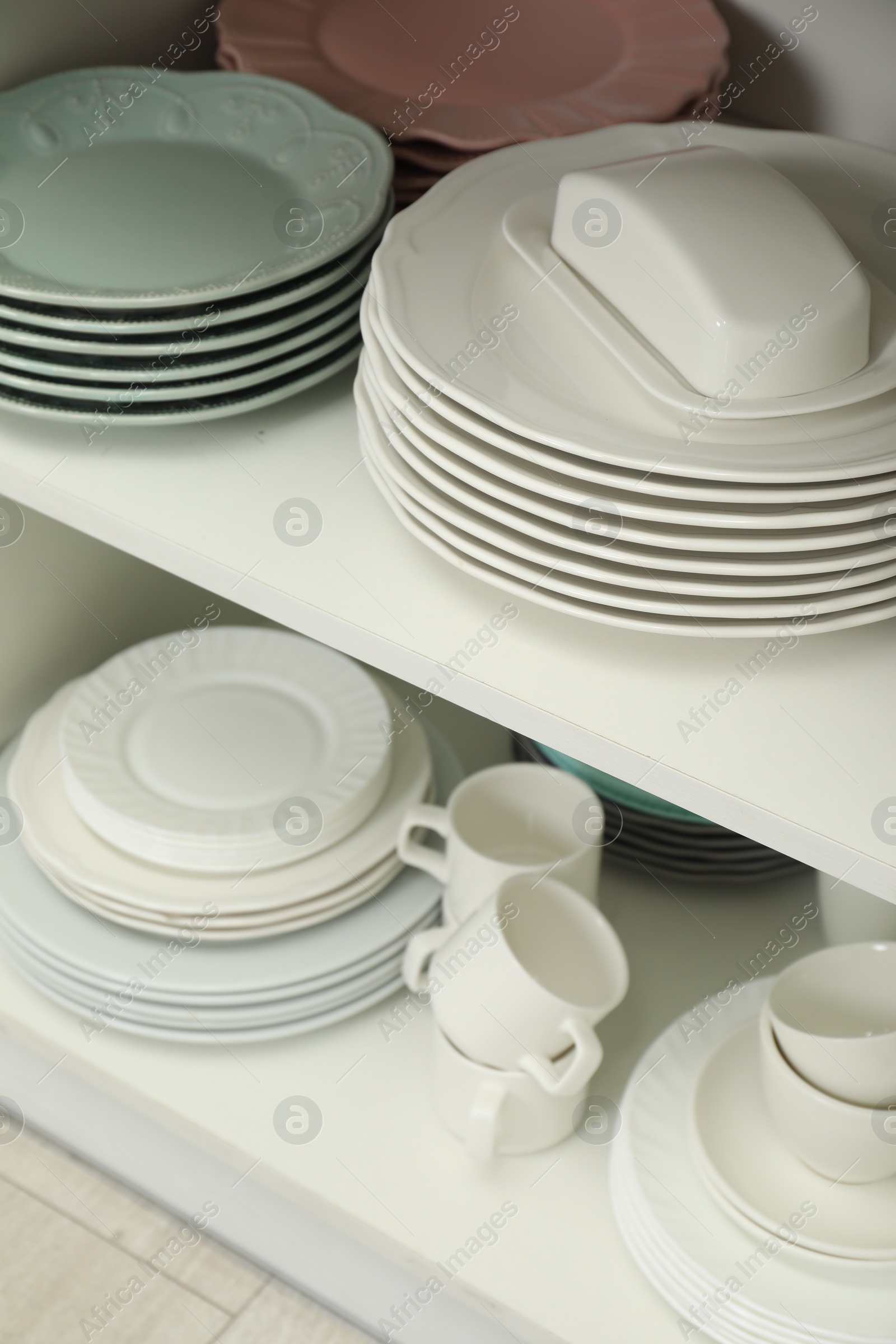 Photo of Clean plates, butter dish and cups on shelves in cabinet indoors