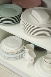 Clean plates, butter dish and cups on shelves in cabinet indoors