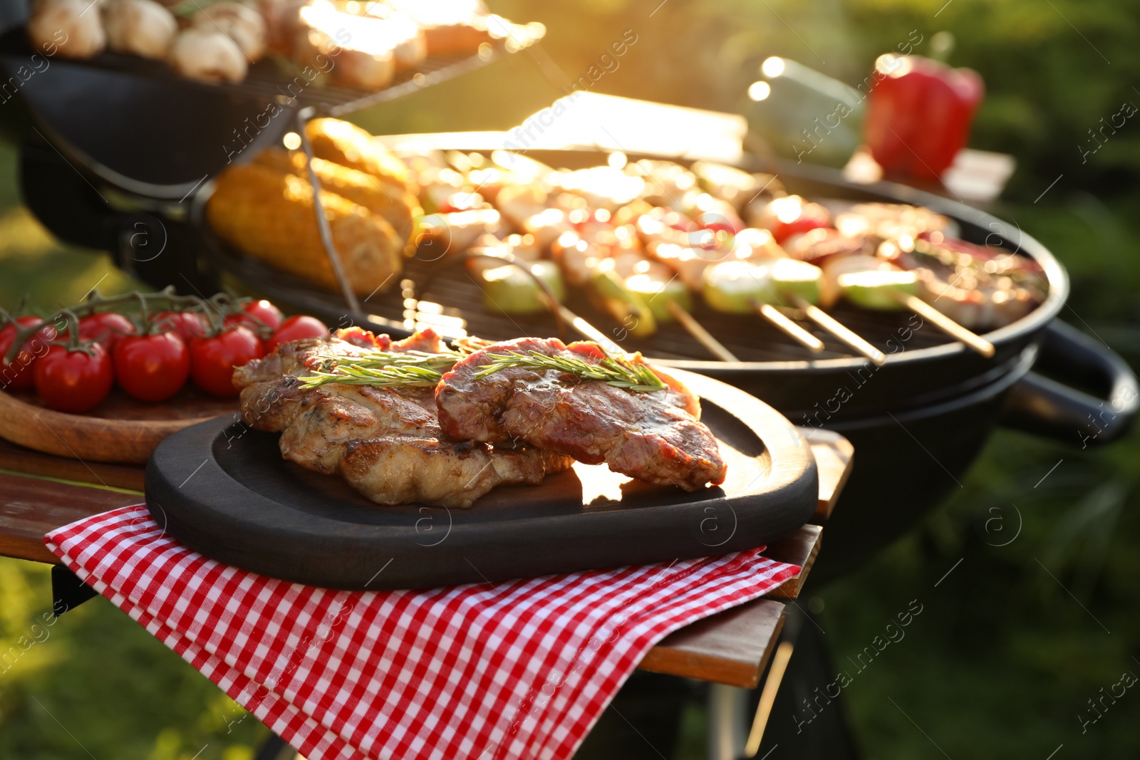 Photo of Tasty cooked meat and cherry tomatoes on table near barbecue grill outdoors