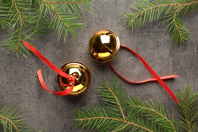 Photo of Golden sleigh bells and fir branches on grey background, flat lay