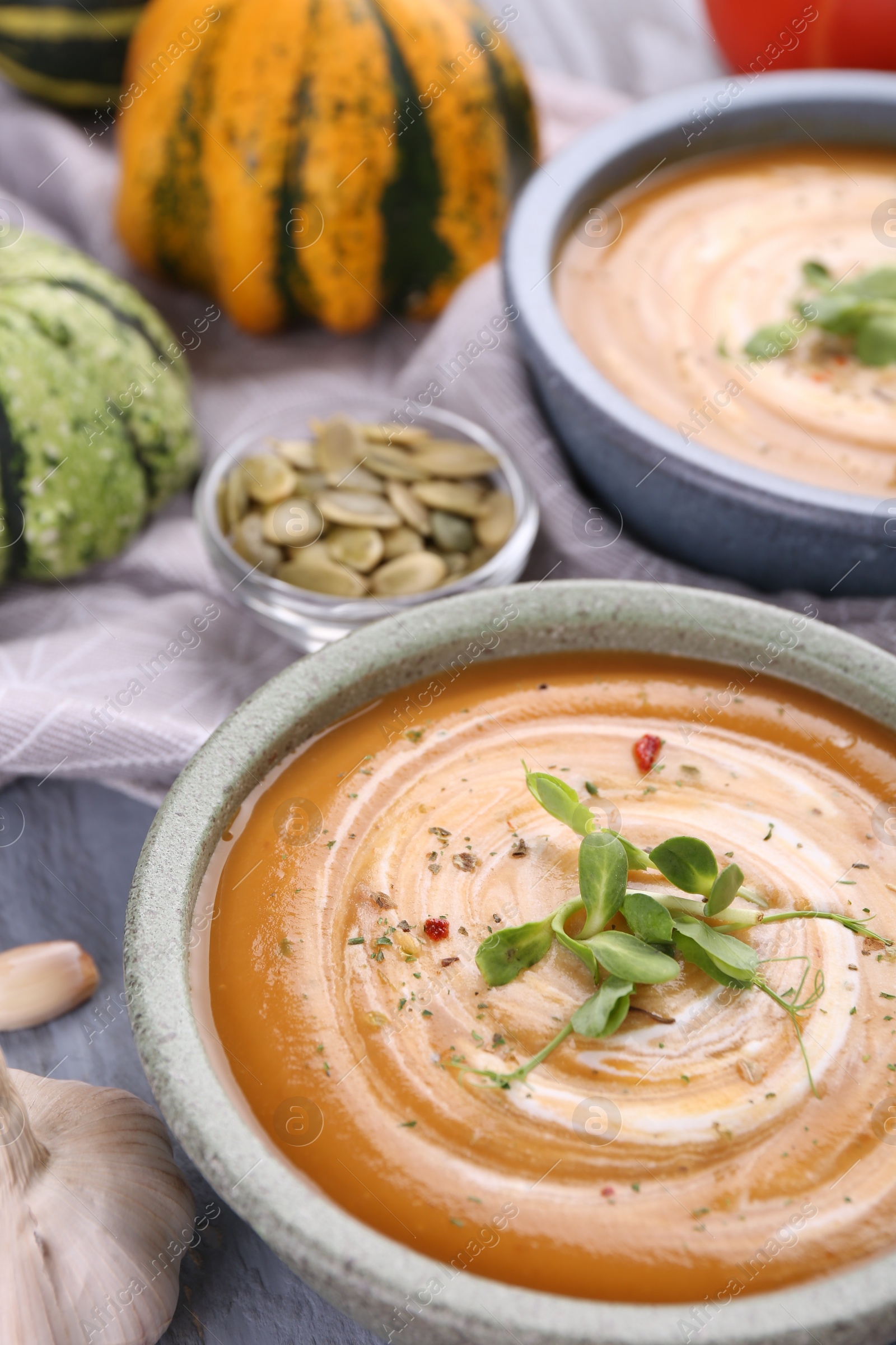 Photo of Delicious pumpkin soup with microgreens in bowls on table, closeup