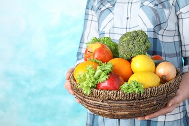 Photo of Woman holding wicker bowl with ripe fruits and vegetables on color background, closeup. Space for text
