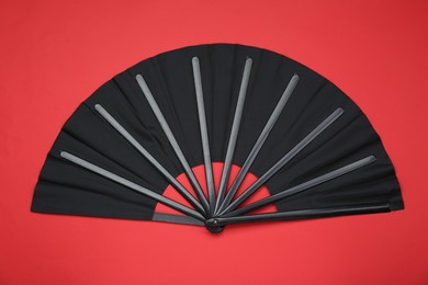 Stylish black hand fan on red background, top view