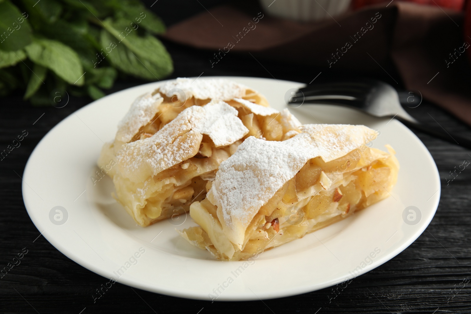 Photo of Delicious apple strudel with almonds and powdered sugar on black wooden table, closeup