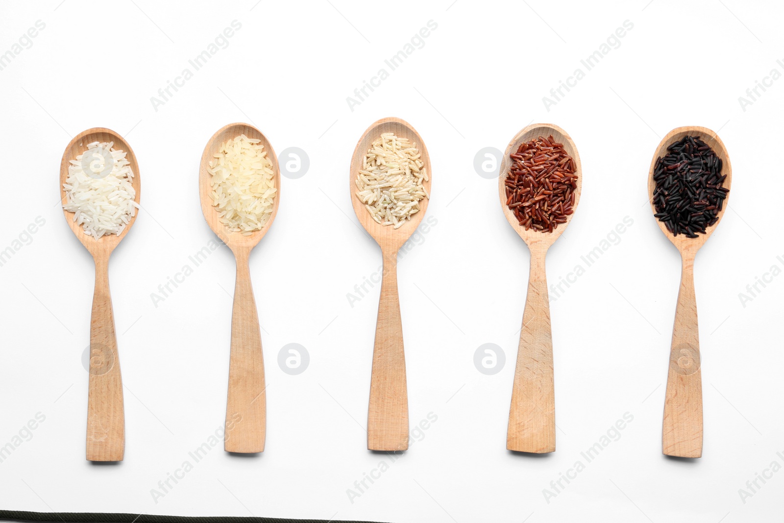 Photo of Spoons with different types of uncooked rice on white background, top view