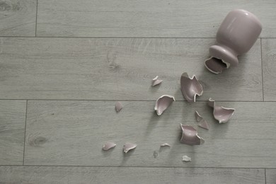 Broken pink ceramic vase on wooden floor, flat lay. Space for text