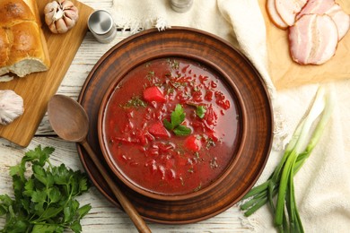 Stylish brown clay bowl with Ukrainian borsch served on white wooden table, flat lay