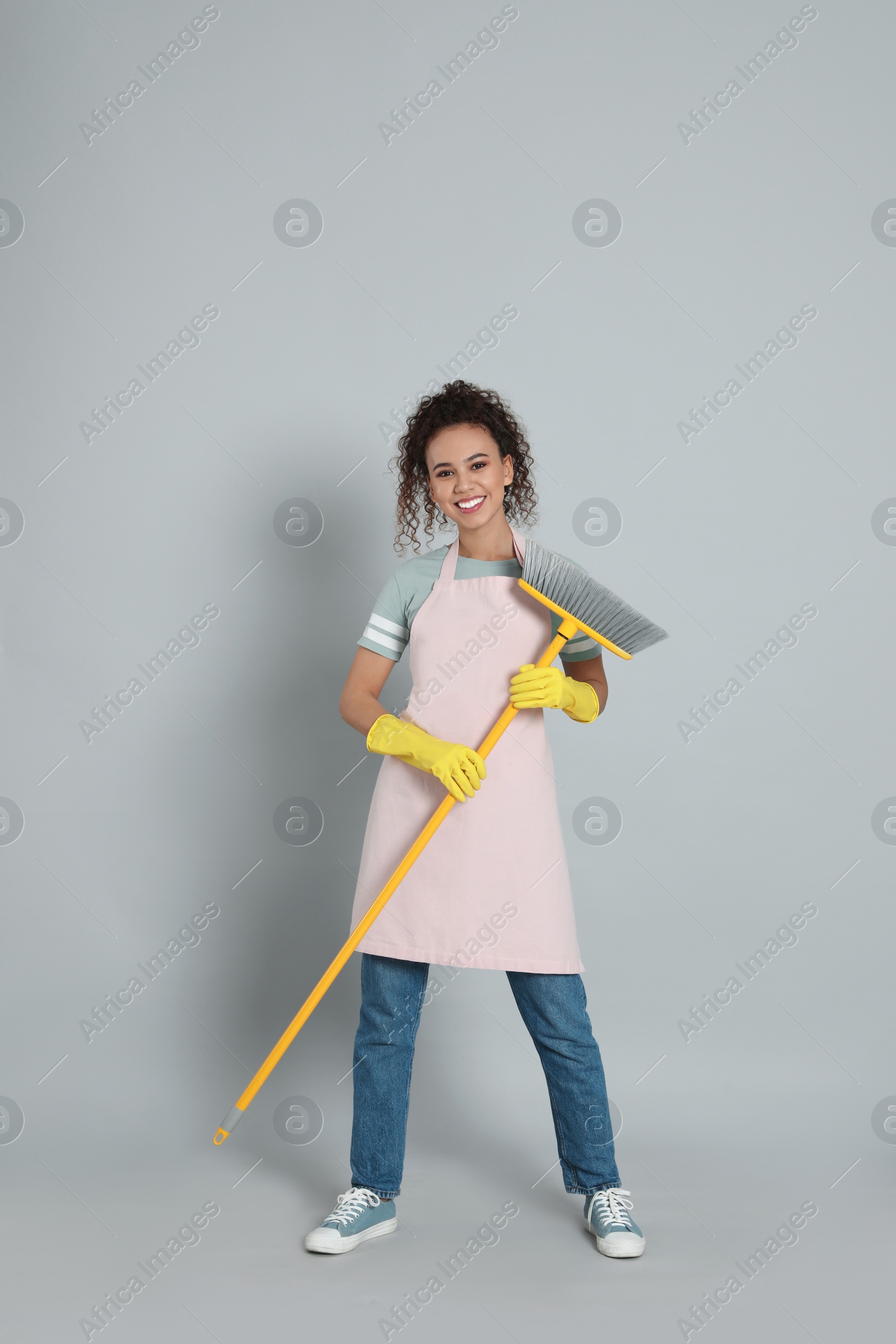Photo of African American woman with yellow broom on grey background