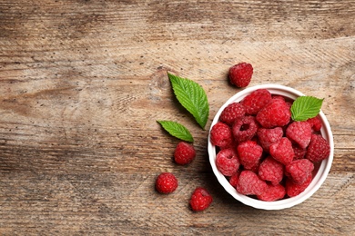 Bowl with delicious ripe raspberries on wooden table, top view. Space for text