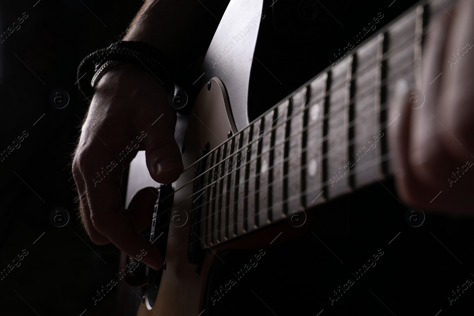 Photo of Man playing electric guitar on black background, closeup. Rock music