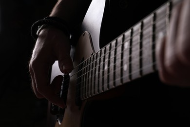 Man playing electric guitar on black background, closeup. Rock music