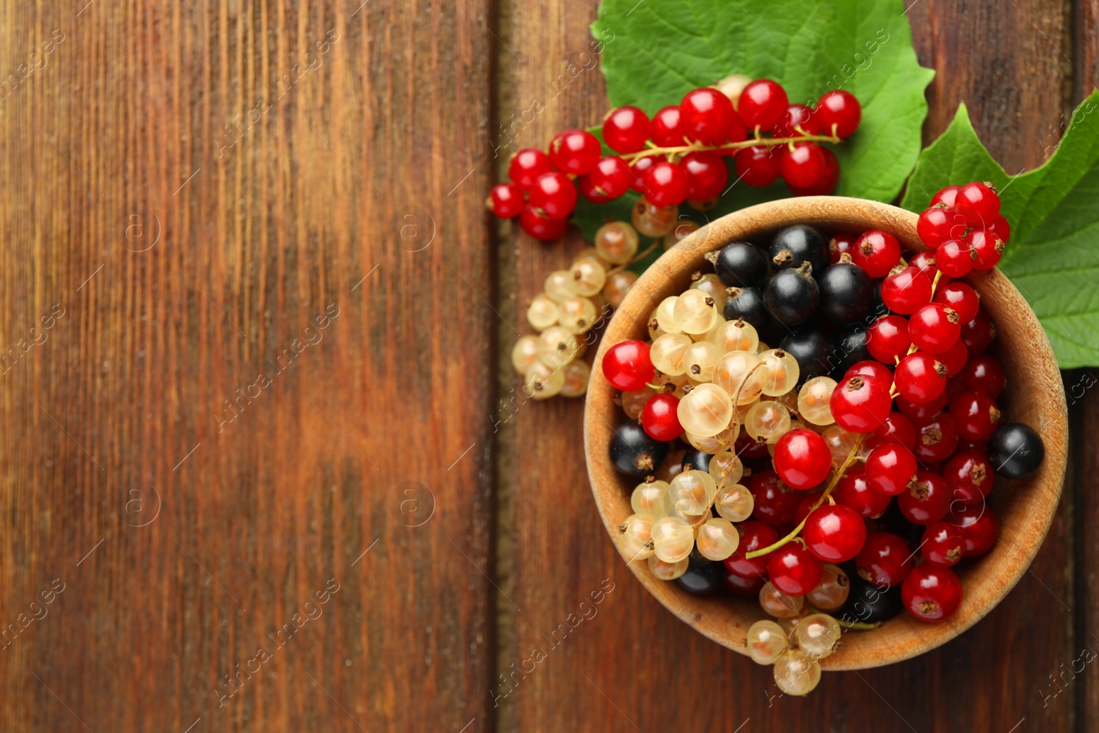 Photo of Different fresh ripe currants and green leaves on wooden table, flat lay. Space for text