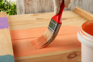 Photo of Worker applying coral paint onto wooden surface, closeup
