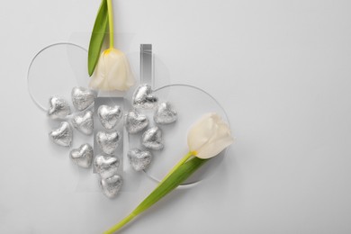 Photo of Heart made with delicious chocolate candies and beautiful tulips on white background, top view. Space for text