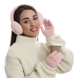 Beautiful young woman in earmuffs with cup of drink on white background