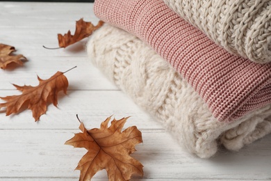 Photo of Stack of folded knitted sweaters and autumn leaves on table. Space for text