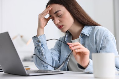 Photo of Woman with glasses suffering from headache at workplace in office