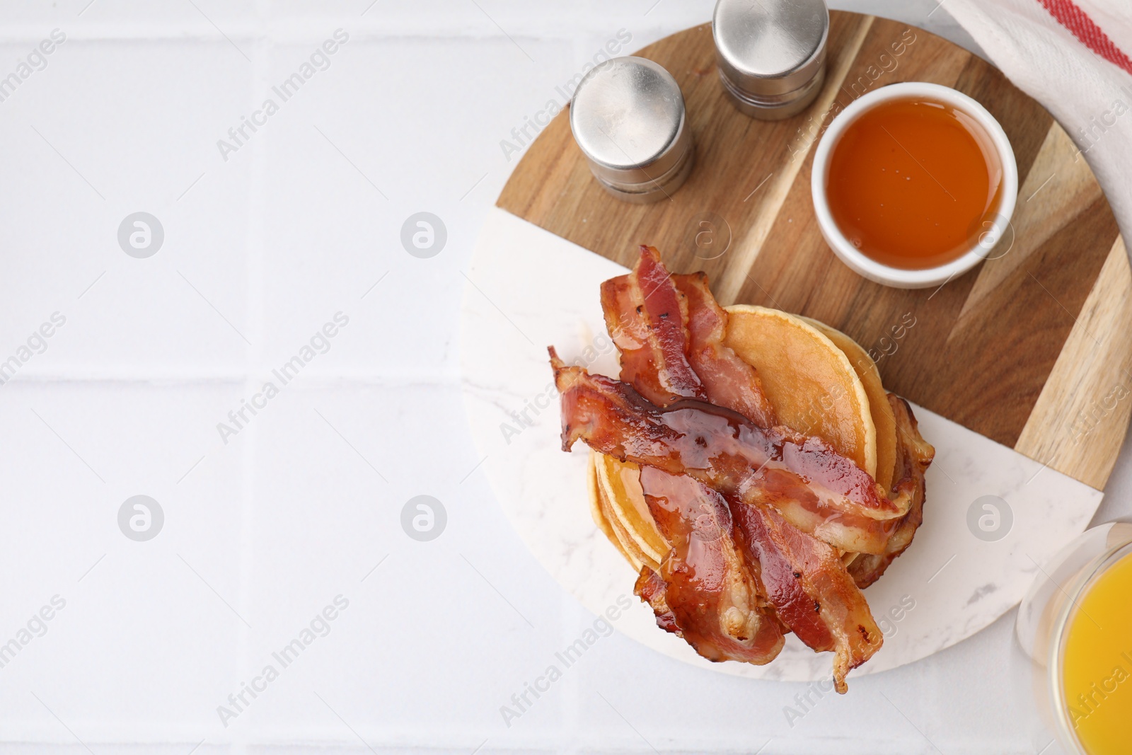 Photo of Delicious pancakes with bacon and honey on white tiled table, top view. Space for text
