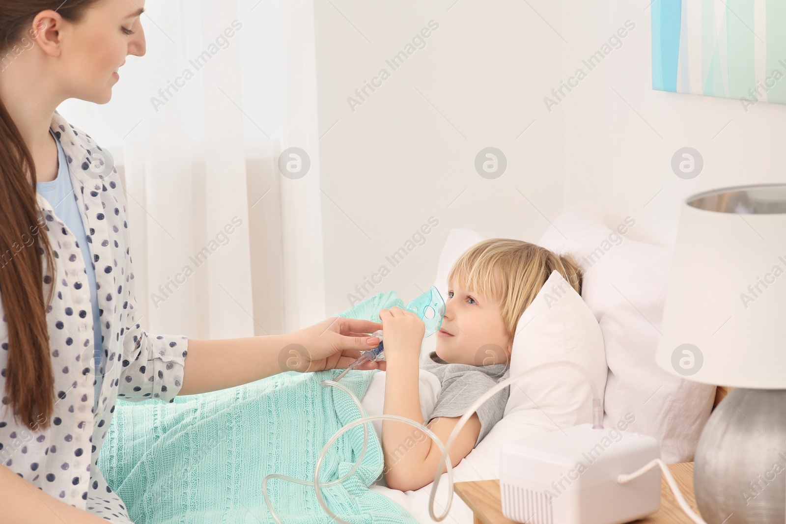 Photo of Mother helping her sick son with nebulizer inhalation in bedroom