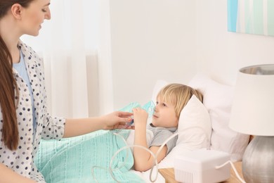 Photo of Mother helping her sick son with nebulizer inhalation in bedroom