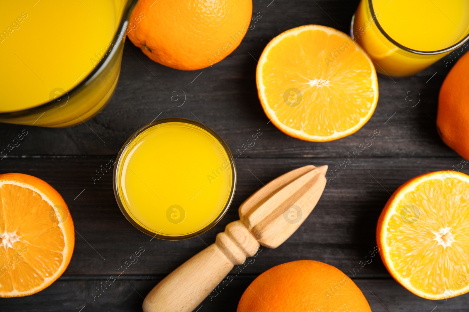 Photo of Fresh ripe oranges, juice and reamer on dark wooden table, flat lay