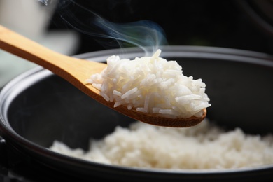 Photo of Spoon with tasty hot rice over cooker, closeup