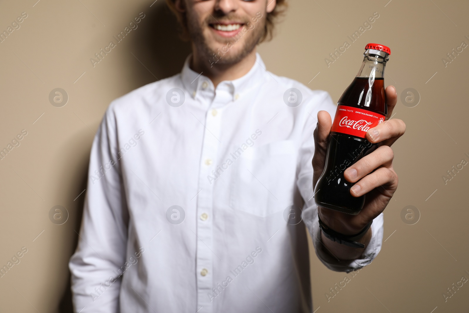 Photo of MYKOLAIV, UKRAINE - NOVEMBER 28, 2018: Young man with bottle of Coca-Cola on color background, closeup