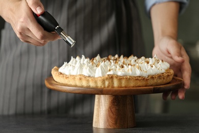 Photo of Woman toasting meringue on lemon pie with kitchen torch at table, closeup