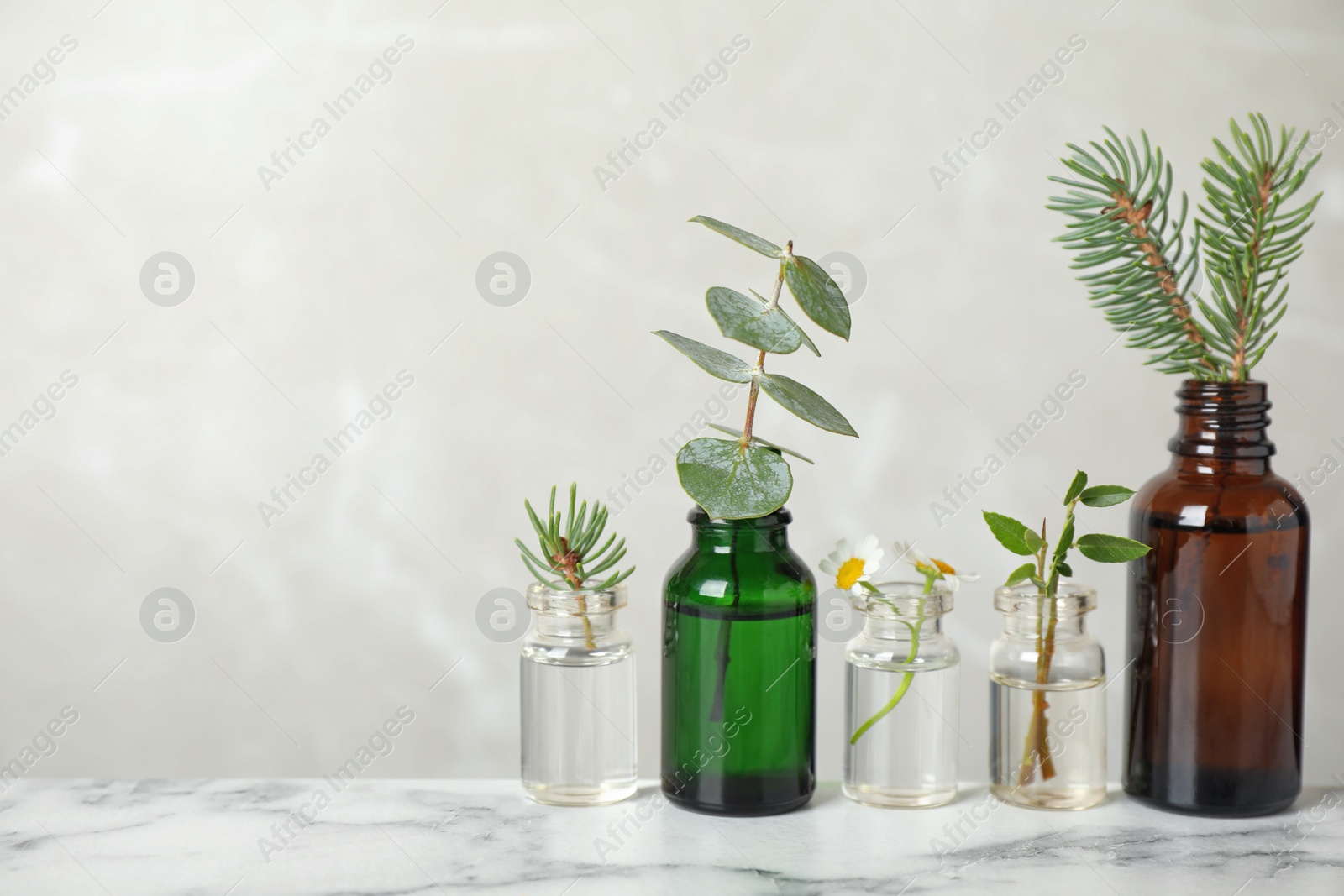 Photo of Glass bottles of different essential oils with plants on table. Space for text