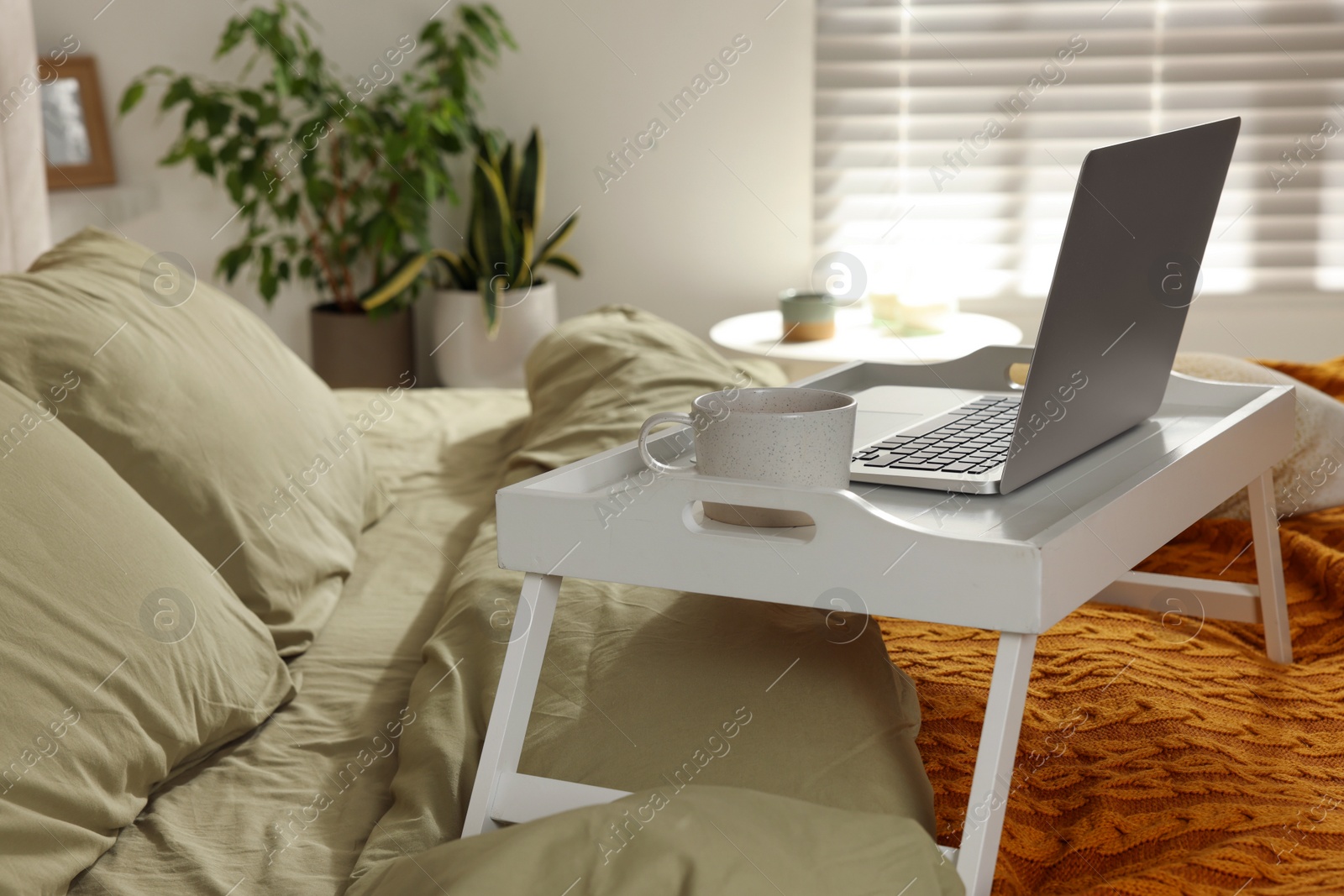 Photo of White tray with modern laptop and cup of aromatic drink on bed indoors, space for text