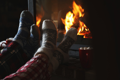Photo of Couple in pajamas resting near fireplace indoors, closeup. Winter vacation